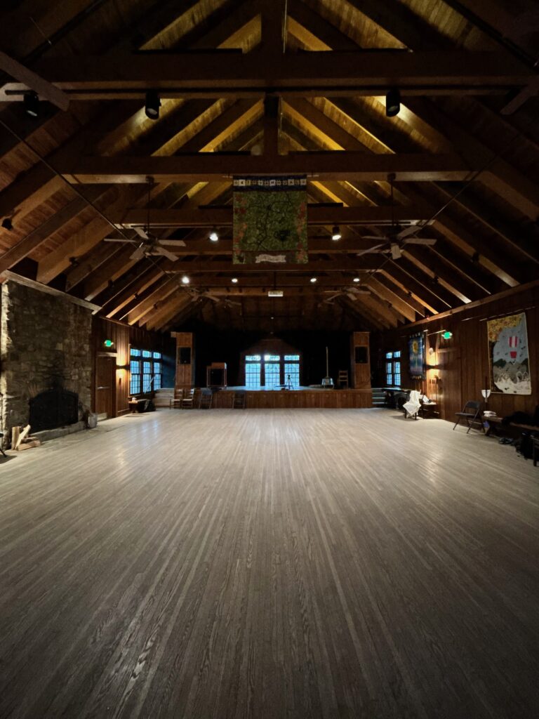 A large empty barn-like structure with high pitched roof and a glossy wooden dance floor.