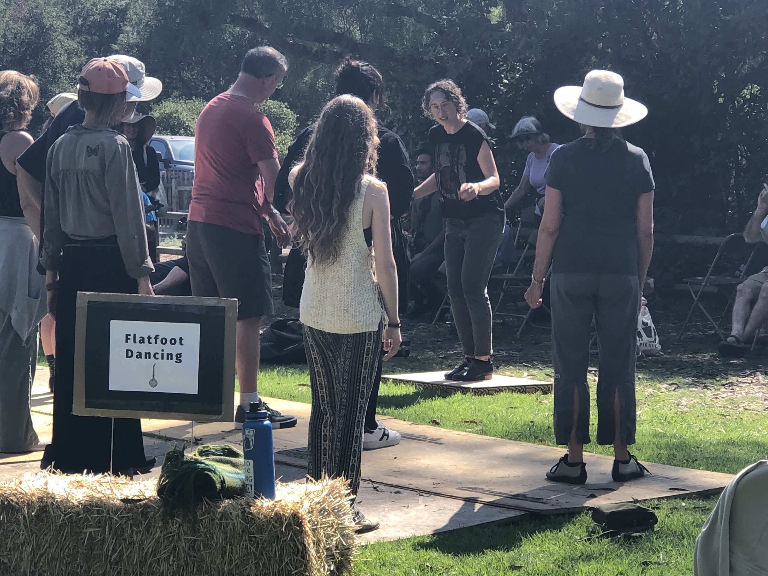 A sign in the lower left reads "flatfoot workshop." A group of people are gathered on wooden boards on a grass lawn, with one person (me) in the front demonstrating a step.